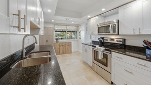 A modern kitchen with white cabinets, stainless steel appliances, and a granite countertop. - Punta Gorda Isles 3 Bedroom Pool Home on Canal (Punta Gorda)