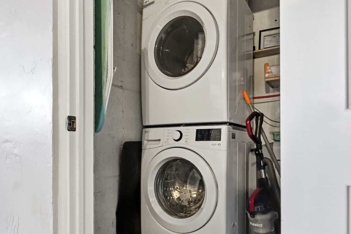 A laundry area with two stacked washing machines and a vacuum cleaner.