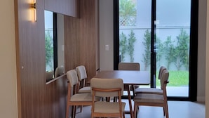 A modern dining area with a wooden table and chairs, a built-in cabinet, and a large window with a view of greenery. - Tranquil 3 Suite Home With Ocean Breeze in Prime Location! (Florianópolis)