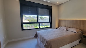 A bedroom with a large window, a bed with a beige bedspread, and a wooden headboard. - Tranquil 3 Suite Home With Ocean Breeze in Prime Location! (Florianópolis)