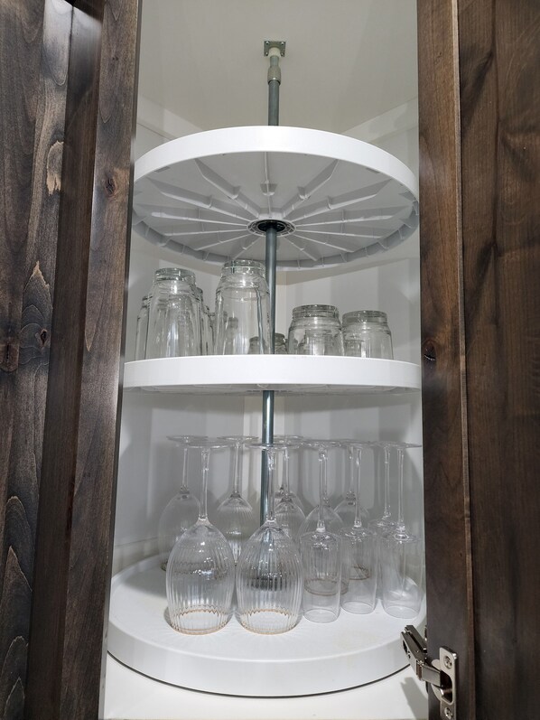 A white, multi-tiered glass display cabinet with clear glassware and jars.
