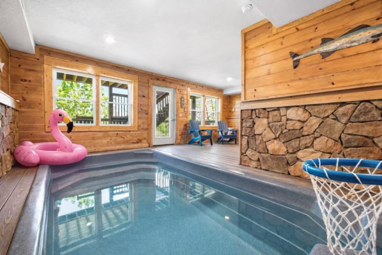 Ein Innenpool mit Steinwand und Holzverkleidung, einem Flamingo-Schwimmpfaugel und einem Basketballkorb.