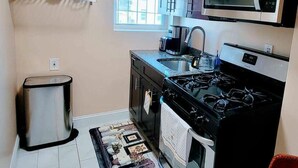 A compact kitchen with dark wooden cabinets, a stainless steel microwave, a gas stove, and a sink. - Vacation Rental In Brooklyn - The Fulton (Brooklyn)