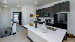 A modern kitchen with dark cabinets, a stainless steel refrigerator, and a white marble countertop.