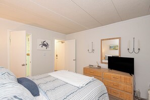 Ein Schlafzimmer mit einem Bett, einer Kommode, einem Fernseher und einer Tür zu einem weiteren Raum.
