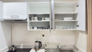 Una cucina compatta con mobili bianchi, forno integrato, bollitore e lavandino.
