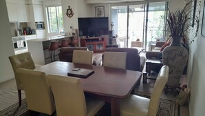 A modern living room with a dining area, a television, and a large window. - Water views luxury 2 bed fully furnished unit (Hope Island)