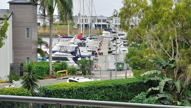 A marina with numerous boats docked, surrounded by residential buildings and lush greenery. - Water views luxury 2 bed fully furnished unit (Hope Island)