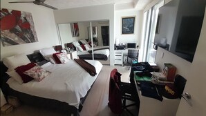 A hotel room with a bed, a desk, a chair, a mirror, and a window. - Water views luxury 2 bed fully furnished unit (Hope Island)