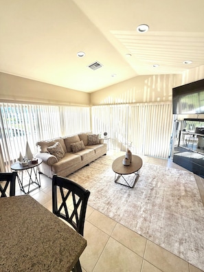 A spacious living room with a beige sofa, a round coffee table, and a dining area with a table and chairs. - Peace Place - House - 2-bedroom in beautiful Coachella (Coachella)