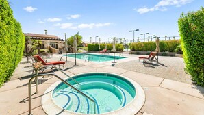 A pool area with two pools, lounge chairs, and a building in the background.