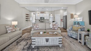 A spacious living room with a sofa, a coffee table, and a patterned armchair. A kitchen is visible in the background. - 4BR ViBe District townhouse, walk to beach, boardwalk & dining. (Virginia Beach)