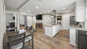 Una cocina moderna con armarios blancos, una isla central y un comedor con mesa y sillas.