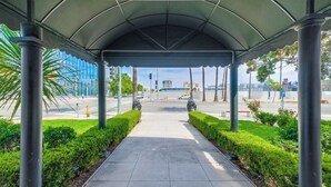 Une allée couverte au design architectural moderne, avec un chemin dégagé bordé de haies verdoyantes et flanqué de deux sculptures en pierre.