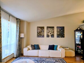 Een woonkamer met een bank, een kamerkleed met dessin en drie wanddecoraties.