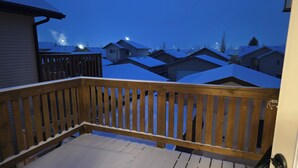 A wooden deck with snow on the railing and a view of snow-covered houses in the background. - Pet friendly 2 bedroom and full bathroom with soaker tub close to Westerner. (Red Deer)
