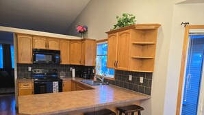 A kitchen with wooden cabinets, a granite countertop, a black stove, and a window with blinds. - Pet friendly 2 bedroom and full bathroom with soaker tub close to Westerner. (Red Deer)