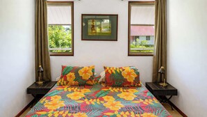 A bed with a floral bedspread, two bedside tables with lamps, and a framed picture on the wall. - Charming 1BR Guesthouse in Beautiful Moorea (Haapiti Tiahura)