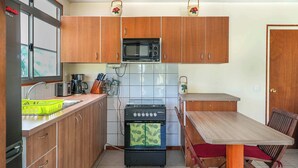A compact kitchen with wooden cabinets, a microwave, a stove, and a dining table with chairs. - Charming 1BR Guesthouse in Beautiful Moorea (Haapiti Tiahura)
