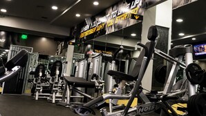 Un gimnasio con diversas máquinas de ejercicio, una pantalla de televisión y carteles de motivación en las paredes.
