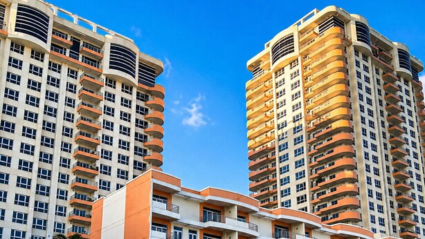 Un edificio residencial alto con varios balcones, techo plano y un cielo azul despejado.