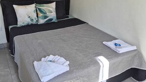 Una cama bien hecha con una colcha gris y almohadas blancas, un cabecero negro y una toalla blanca pequeña al lado.