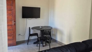 A living room with a black sofa, a round table with chairs, a ceiling fan, and a TV mounted on the wall.