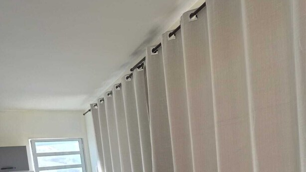 Una sala moderna con un sofá negro, una mesita y una ventana con persianas verticales.