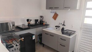 Una cocina compacta con microondas, cafetera y refrigerador pequeño.