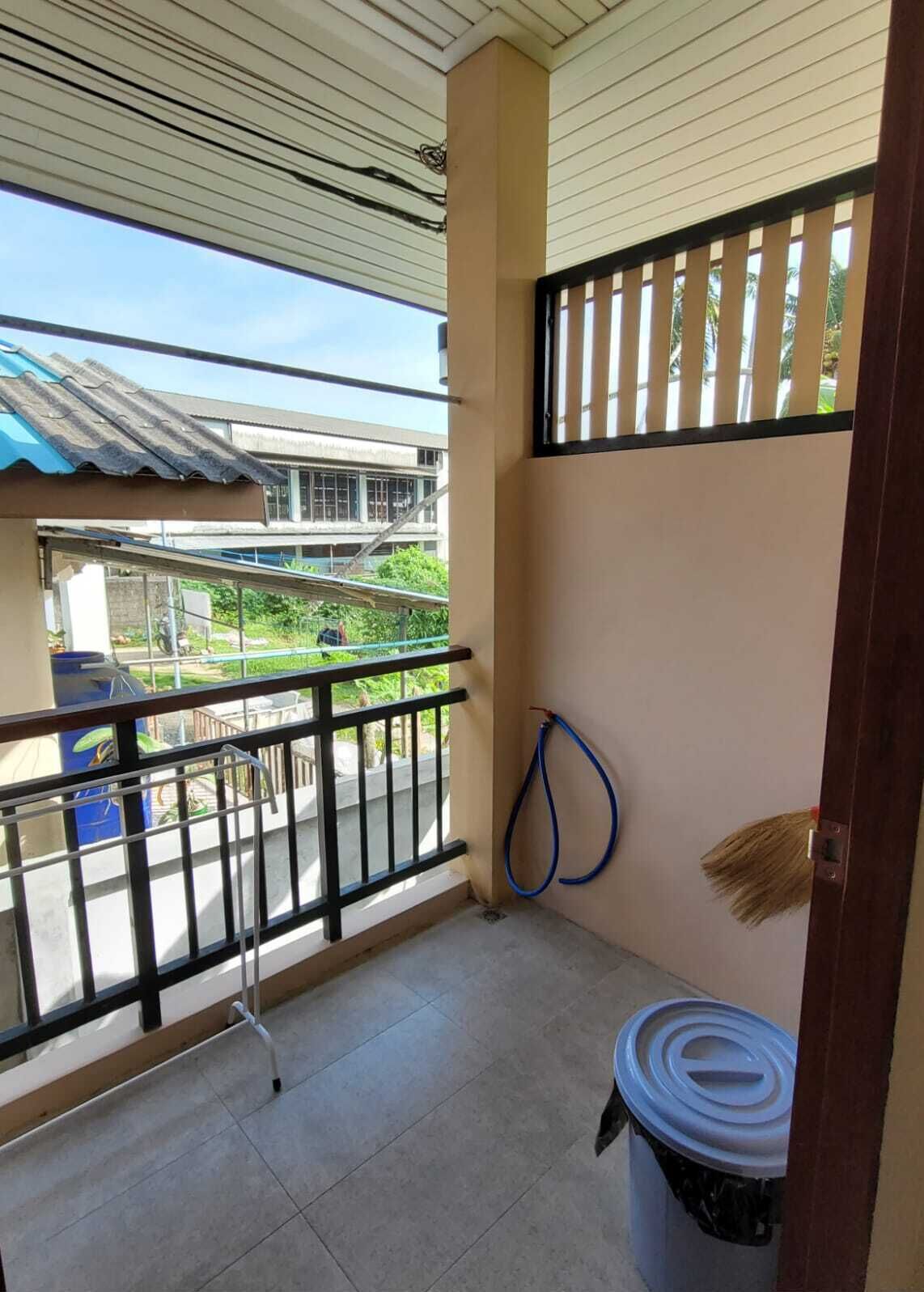 A balcony with a metal railing, a blue hose, and a trash bin.