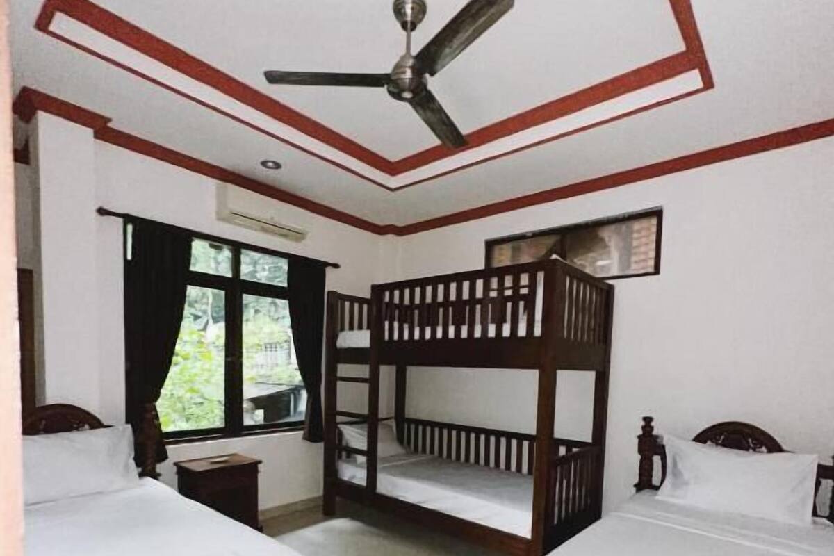 A room with two wooden beds, a ceiling fan, and a window with curtains.