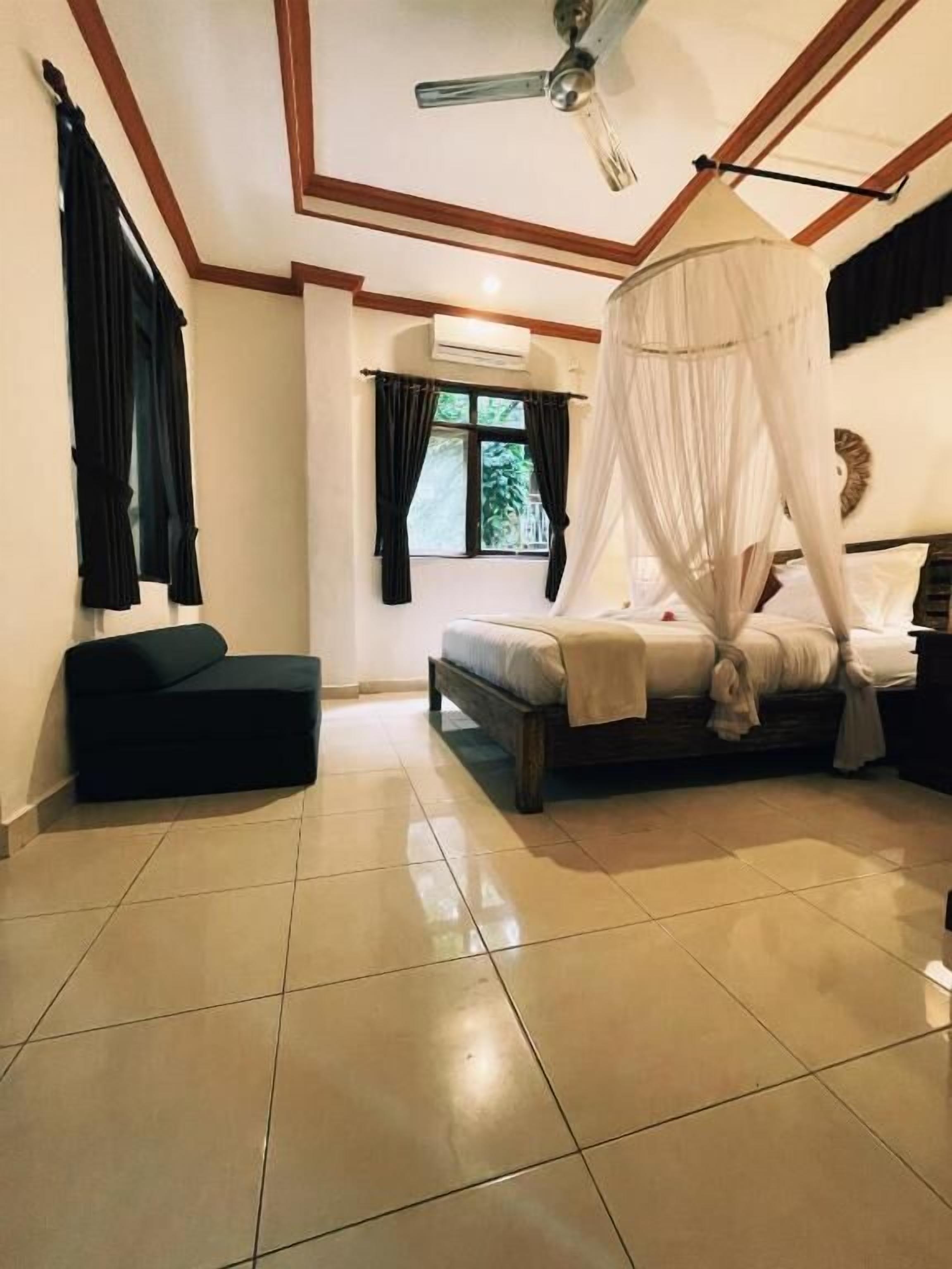 A bedroom with a bed under a canopy, a ceiling fan, and a window with curtains.