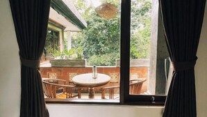 A window with black curtains, a round table, and chairs outside. - The Nest in Ubud (Ubud)
