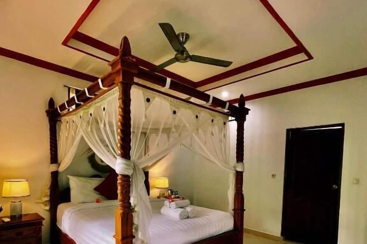 A four-poster bed with a canopy, a ceiling fan, and a tiled floor.