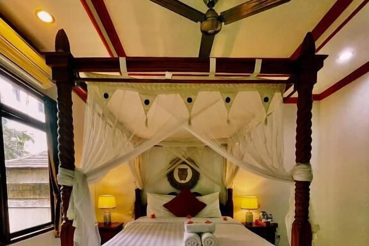 A four-poster bed with a canopy, a ceiling fan, and a nightstand with a lamp.
