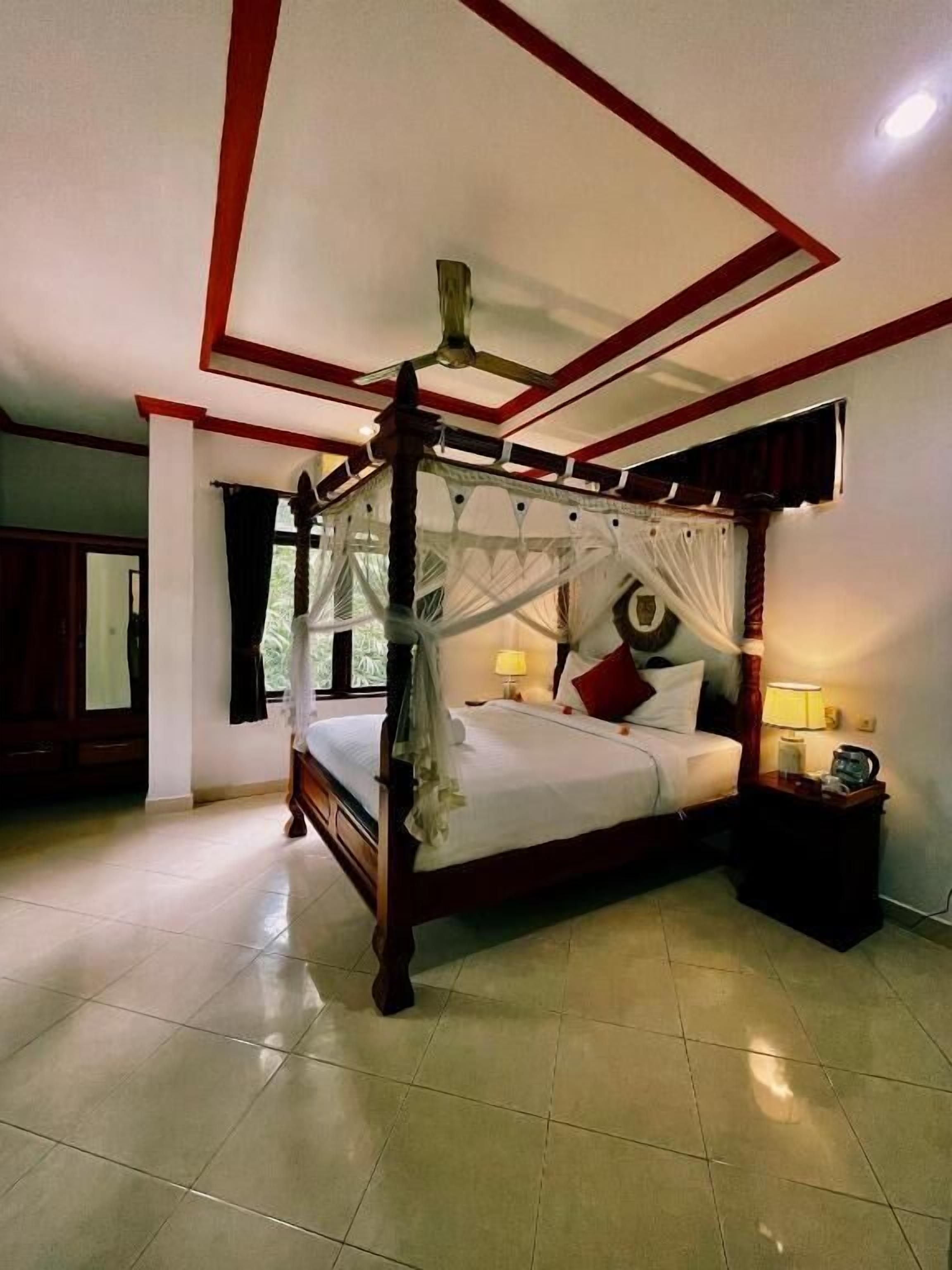 A four-poster bed with a canopy, a ceiling fan, and a nightstand with a lamp.