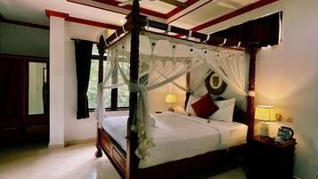 A four-poster bed with a canopy, a ceiling fan, and a nightstand with a lamp.