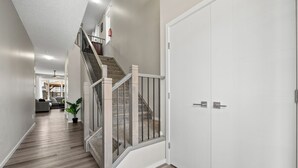 A modern hallway with a wooden floor, a staircase with metal railings, and a white door.