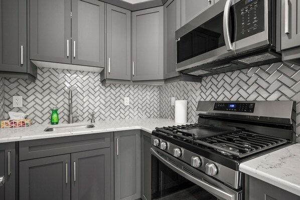 A modern kitchen with grey cabinets, a stainless steel stove, a microwave, and a herringbone-patterned backsplash. - Bright & Spacious Family Retreat (Calgary)
