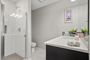 Un baño moderno con mampara de vidrio, inodoro, lavabo con espejo y un cuadro en la pared.