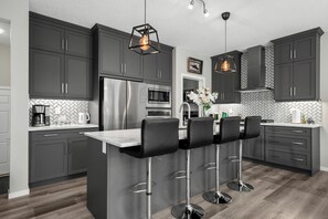 A modern kitchen with dark cabinets, stainless steel appliances, and a central island with bar stools. - Bright & Spacious Family Retreat (Calgary)