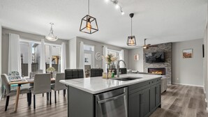 A modern kitchen with a central island, dining area with chairs, and a fireplace.