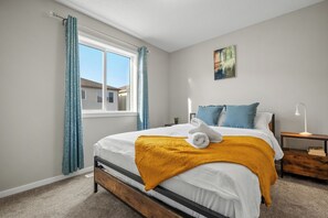 Un dormitorio con cama, ventana, mesita de noche y un cuadro en la pared.
