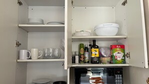 A kitchen with white cabinets, a microwave, and various kitchen items like plates, cups, and bottles. - Nest Aparthotel kitchenette  (New York)