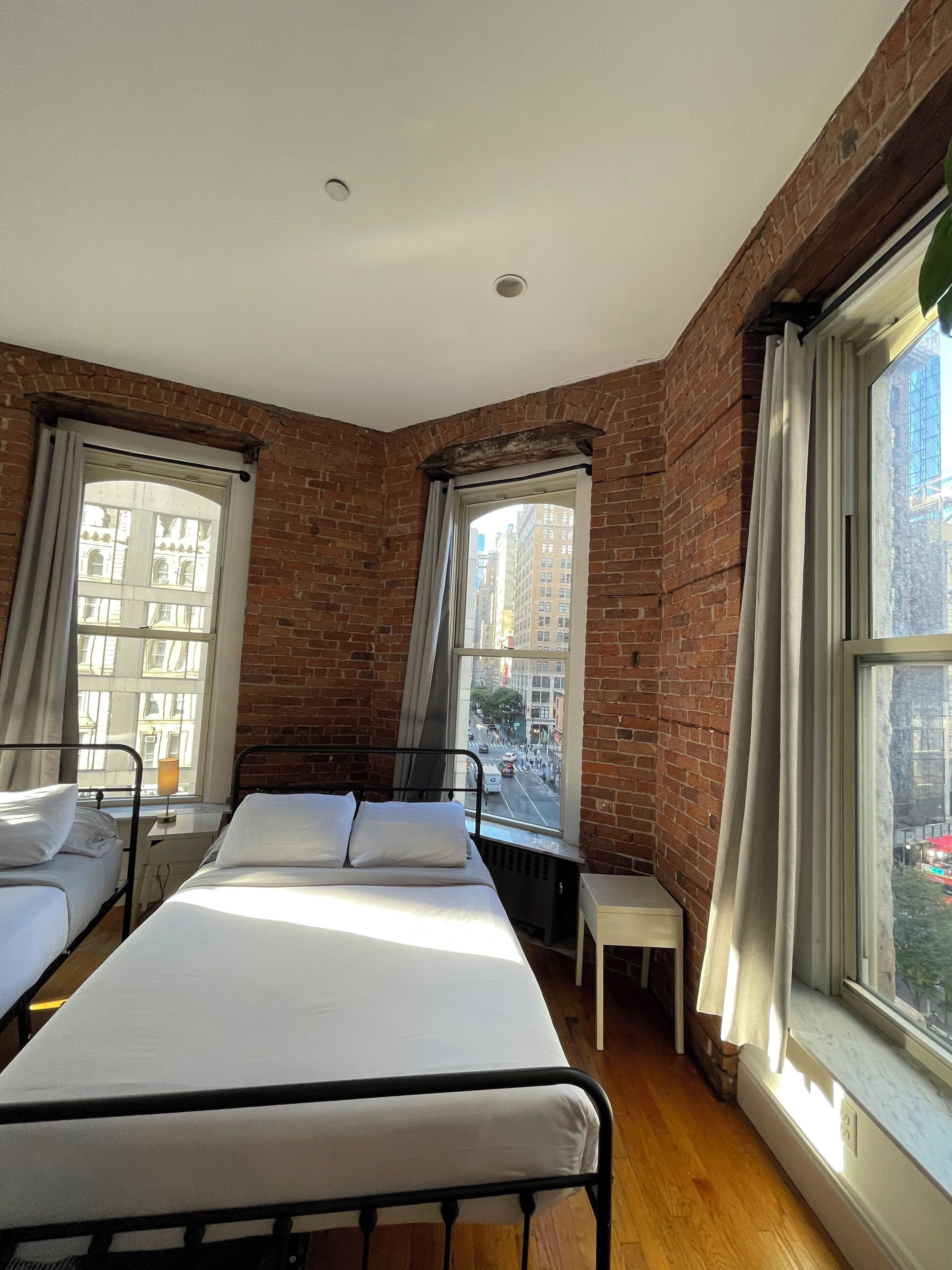 Una habitación con dos camas, una mesita y ventanas amplias con cortinas.