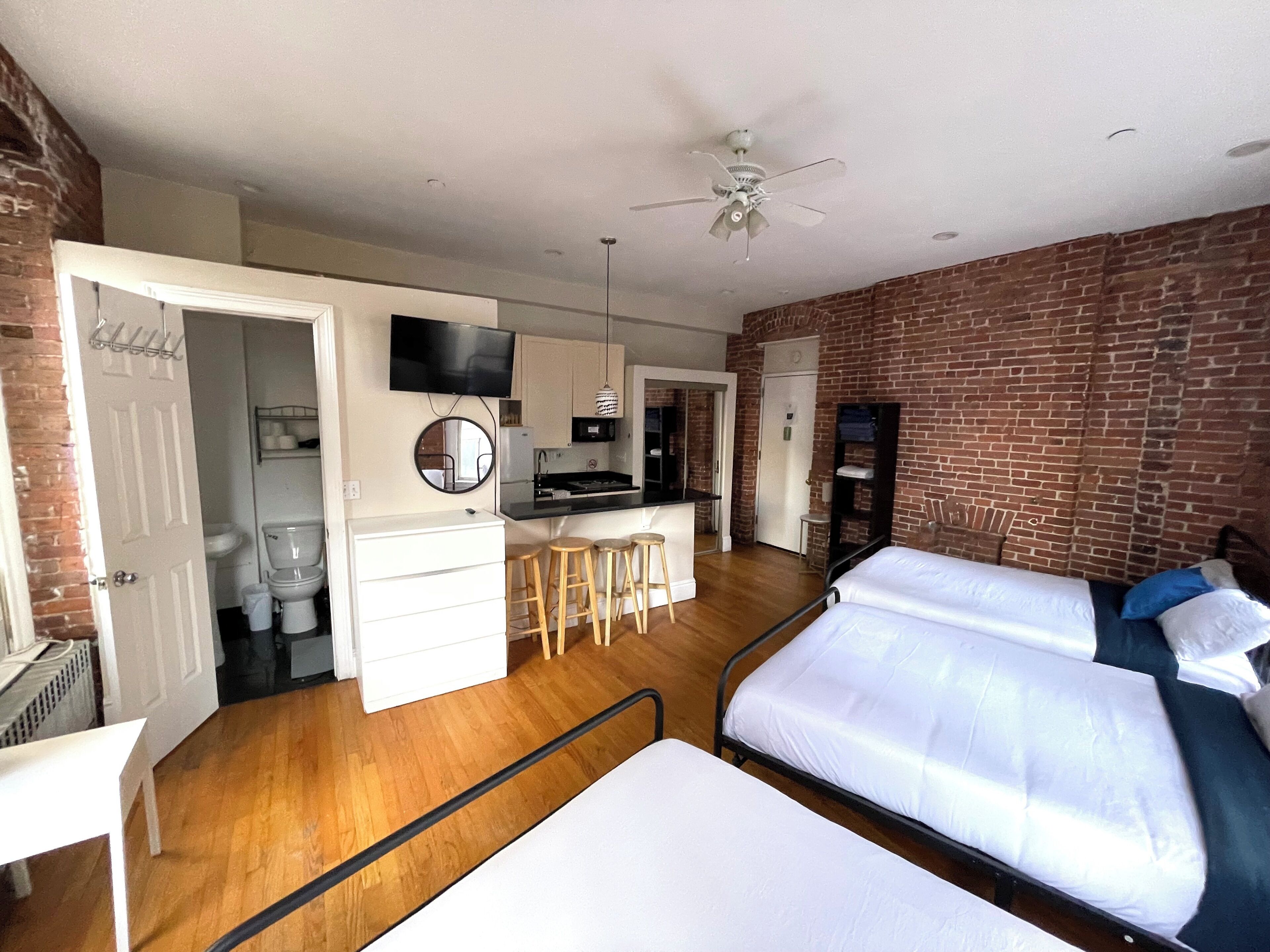 A compact hotel room with a kitchenette, a bed, a desk, and a bathroom.