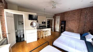 A compact hotel room with a kitchenette, a bed, a desk, and a bathroom.