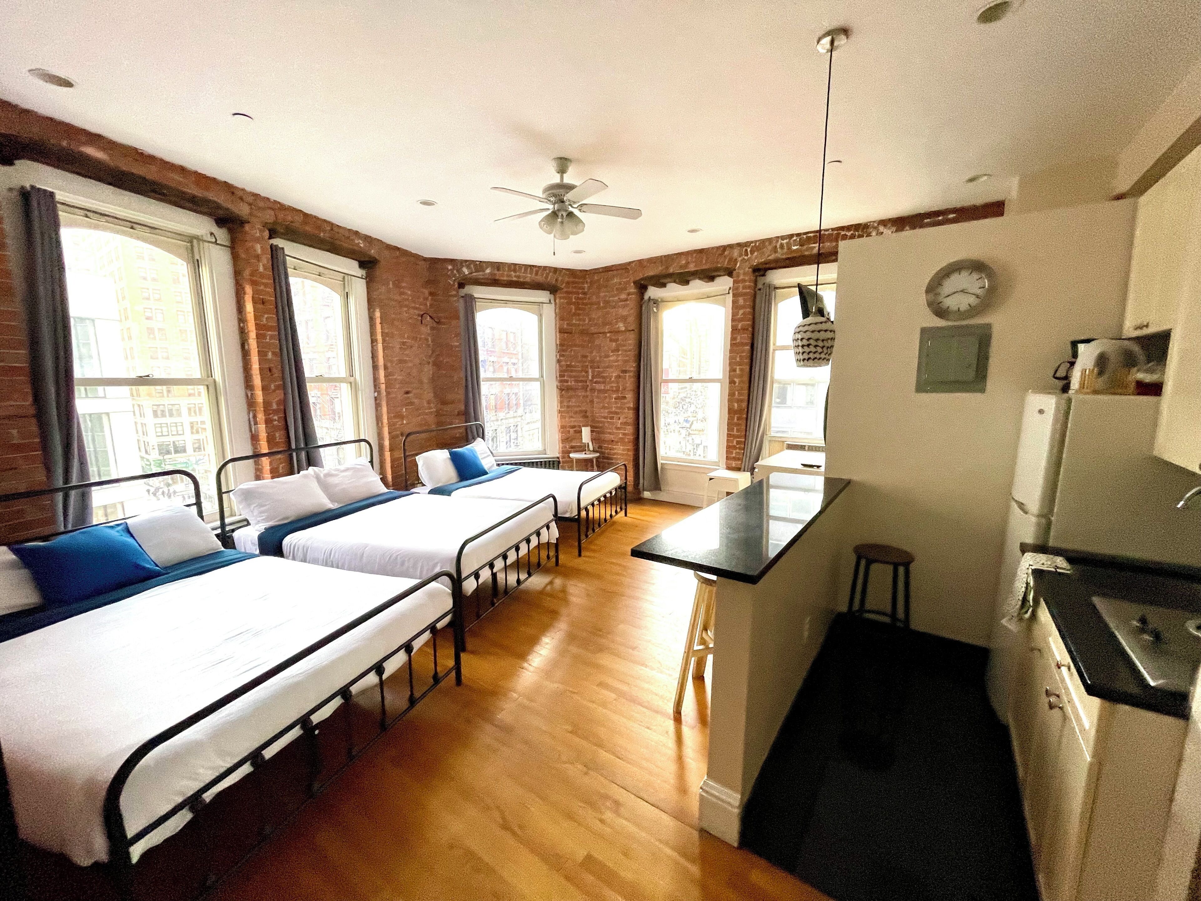Una habitación con dos camas individuales, un pequeño rincón de cocina y una ventana con vistas a edificios.