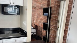 A kitchen with a black countertop, white cabinets, and a microwave. There is a brick wall and a door leading to another room. - Nest Aparthotel kitchenette  (New York)
