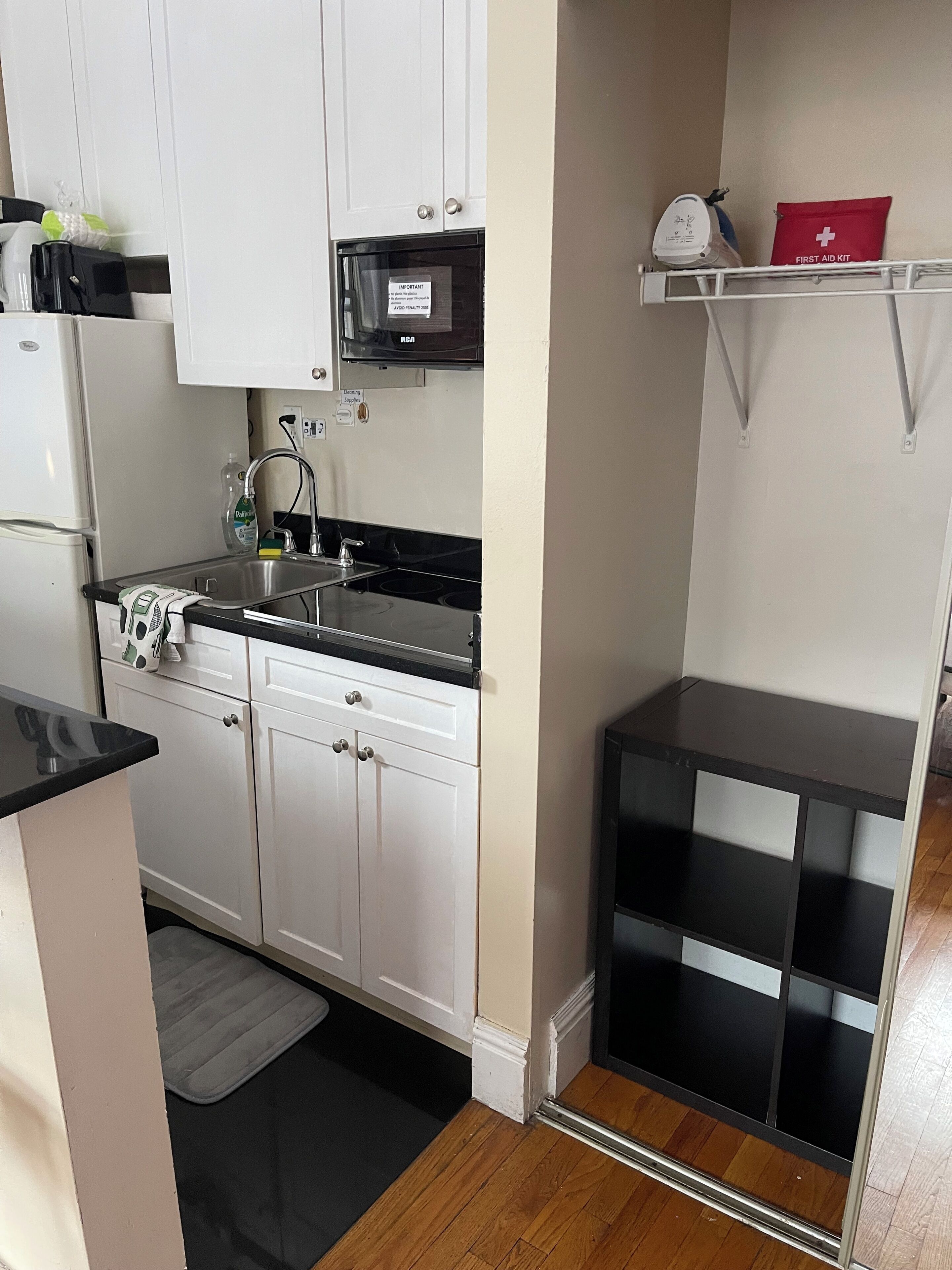 Una cocina compacta con armarios blancos, una encimera negra, un microondas, un lavabo y un botiquín en un estante.